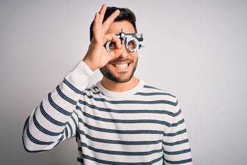 Young handsome man with beard wearing optometry glasses over isolated white background doing ok gesture with hand smiling, eye looking through fingers with happy face.