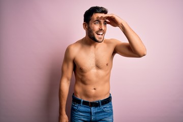 Fototapeta premium Young handsome strong man with beard shirtless standing over isolated pink background very happy and smiling looking far away with hand over head. Searching concept.