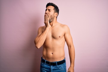 Fototapeta premium Young handsome strong man with beard shirtless standing over isolated pink background bored yawning tired covering mouth with hand. Restless and sleepiness.
