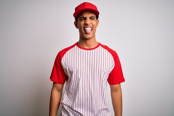 Young handsome african american sportsman wearing striped baseball t-shirt and cap sticking tongue out happy with funny expression. Emotion concept.