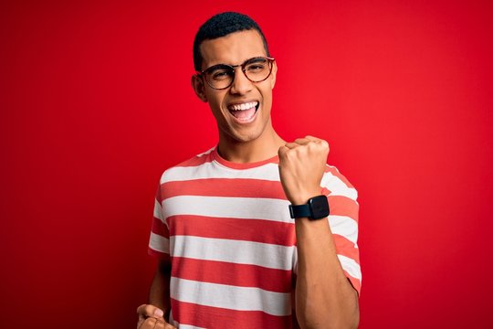 Young handsome african american man wearing casual striped t-shirt and glasses celebrating surprised and amazed for success with arms raised and eyes closed. Winner concept.