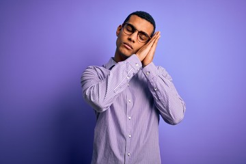 Fototapeta premium Handsome african american man wearing striped shirt and glasses over purple background sleeping tired dreaming and posing with hands together while smiling with closed eyes.