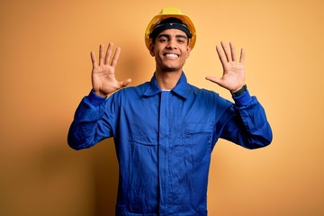 Young handsome african american worker man wearing blue uniform and security helmet showing and pointing up with fingers number ten while smiling confident and happy.