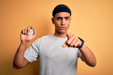 Young handsome african american man doing sport using stopwatch over yellow background pointing with finger to the camera and to you, hand sign, positive and confident gesture from the front