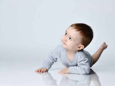 Little baby boy toddler in grey casual jumpsuit and barefoot lying on floor, smiling and looking up