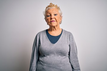 Senior beautiful grey-haired woman wearing golden queen crown over white background Relaxed with serious expression on face. Simple and natural looking at the camera.