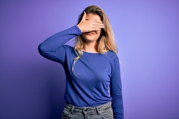 Young beautiful blonde woman wearing casual t-shirt over isolated purple background covering eyes with hand, looking serious and sad. Sightless, hiding and rejection concept