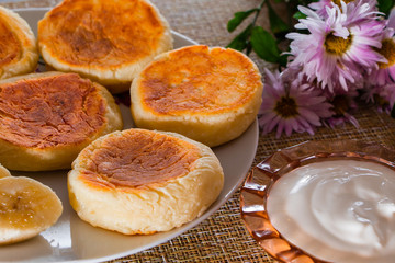 Naklejka na ściany i meble Cheesecakes on a plate on a brown background. Dish of cottage cheese for breakfast.