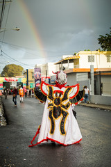 person in black spider costume pass by city street against rainbow on dark sky