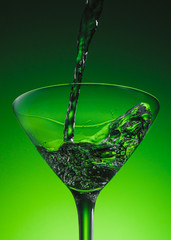 Martini pouring in a cocktail glass with splash. Extra dry martini. Vermouth wine. Alcohol cocktail Beautiful green emerald background. 