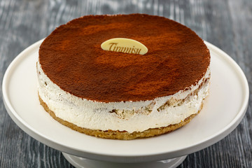 Dessert tiramisu cake with mascarpone, savoyardi cookies and amaretto liqueur on a white plate of gray wooden background