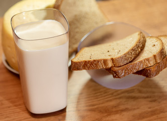 A glass of milk and a piece of cheese and slices of rye bread under a yellowed wooden table