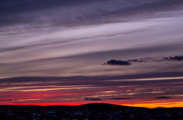 Brightly colorful sunset sky with clouds against the background of the dark silhouette of the village. Beautiful colorful sunset over the winter outlines of houses. Russia