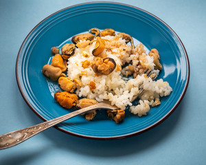 Close-up rice with mussels in a blue ceramic plate and a table fork