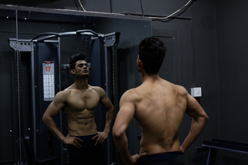 Fototapeta na wymiar An young and handsome Indian Bengali brunette man and his mirror image with muscular body doing exercise in a multi gym. Fitness and Indian lifestyle.