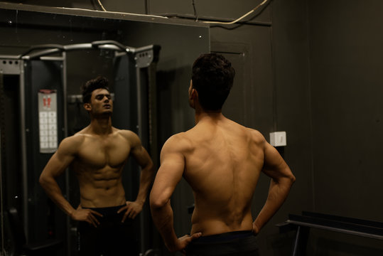 An young and handsome Indian Bengali brunette man and his mirror image with muscular body doing exercise in a multi gym. Fitness and Indian lifestyle.