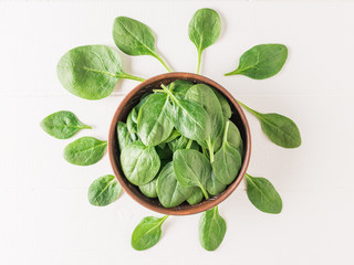 A bowl of fresh spinach leaves on a white wooden table. Food for fitness. The view from the top.