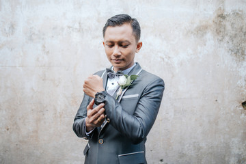 Selective focus of groom is standing with concrete wall background. Wedding concept.