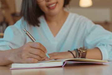 Woman hand writing down in small white memo notebook for take a note not to forget or to do list plan.