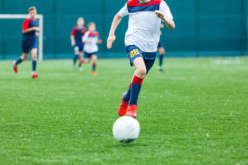 Boys in white and blue sportswear plays  football on field, dribbles ball. Young soccer players with ball on green grass. Training, football, active lifestyle for kids concept 