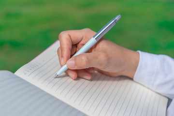 Woman hand writing down in small white memo notebook for take a note not to forget or to do list plan.