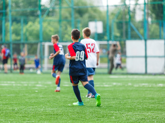 Obraz premium Boys in white and blue sportswear plays football on field, dribbles ball. Young soccer players with ball on green grass. Training, football, active lifestyle for kids concept 