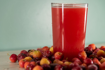 Glass of acerola juice and fresh acerola fruits on a wooden surface