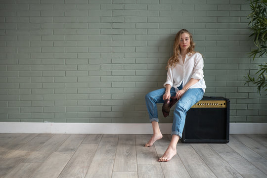 Young beautiful woman sitting on subwoofer with bare feet next to green plant