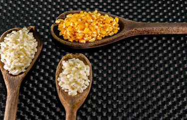 Milho de cor branca e amarela para preparar canjica servida em colheres de madeira sobre um fundo escuro