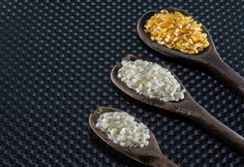 Milho de cor branca e amarela para preparar canjica servida em colheres de madeira sobre um fundo escuro