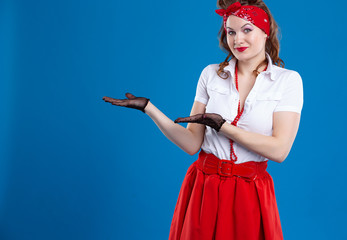 A young happy smiling woman dressed in pin-up style showing something or a copyspace area for a...