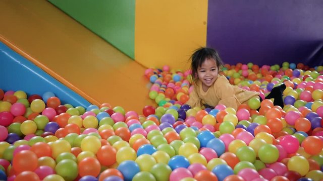 Cute little child girl having fun to playing slide in plastic dry pool with colorful balls Inside the kids playground indoor.