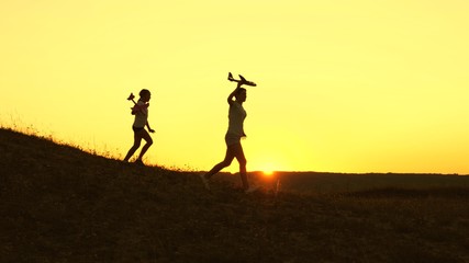 Dreams of flying. Happy childhood concept. Two girls play with a toy plane at sunset. Children on background of sun with an airplane in hand. Silhouette of children playing on plane