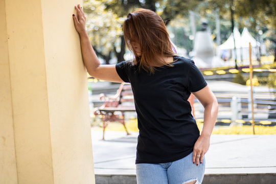 Young woman wearing black t shirt posing at park in front view, suitable for mock up template, background, etc.