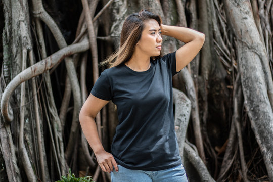Young woman wearing black t shirt posing at park in front view, suitable for mock up template, background, etc.