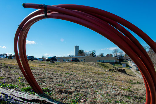 A Water Tower and Trees off in the distane Through a Loop of Red Piping With a Field of Dirt in the foreground