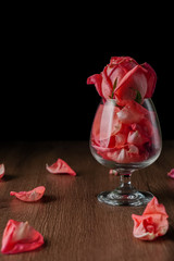 a group of pink roses put in wine glass that falling on dark color wooden table