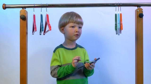  Cute blond boy in green sweater at home. a teenager climbed into locker room took smartphone and sings among empty hangers