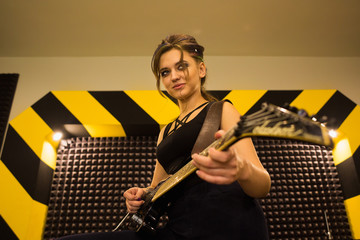 young beautiful tattooed girl with a guitar, rock singer recording the sound in professional studio on the striped wall