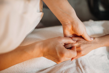 Young masseur is massaging woman's fingers to make them relaxed after spa sessions