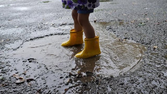 slow motion kid wearing yellow boot playing water rain puddle on road
