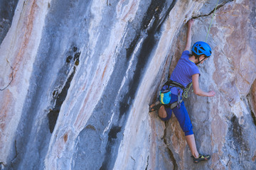 A woman in a helmet climbs a beautiful blue rock.