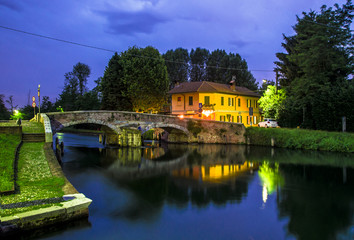 Fototapeta na wymiar medieval stone bridge with two arches in a countryside location on the outskirts of Milan. night view of the river.