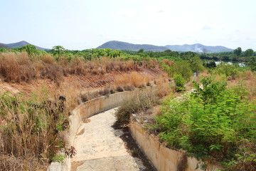 Concrete irrigation canals that are dry and without water during drought with mountain and blue sky in background, Forests and weeds that change color from green to brown, Thailand