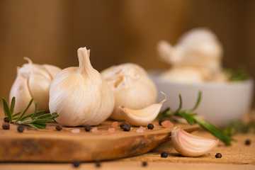Spicy fresh garlic with rosemary and thyme and black pepper. Culinary splash, on a wooden background.