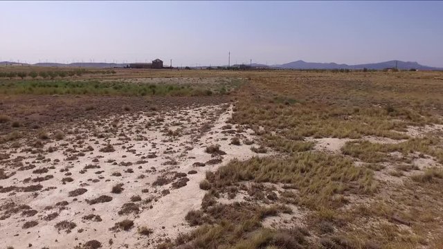 Dry landscape view from the air.  A patch of dry sand is seen first and after some dry grass bushes. Also some buildings far on the horizon.Camera moves forward