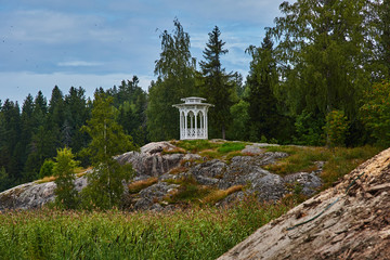Lonely gazebo on the hill.White open summer round veranda in the park of the city of Sortavala: a forest of conifers, traces of volcanic lava, rocks and volcanic rocks. Russia, Karelia, Sortaval