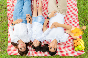 Asian teen family happy holiday picnic moment in the park with father, mother and daughter lying on mat and smile to happy spend vacation time togerter in green garden with friut and food..