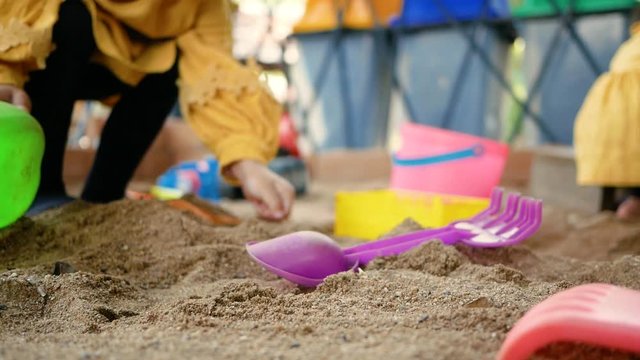 Happy little child girl having fun playing with plastic toys sitting in the sandbox on a sunny summer day.