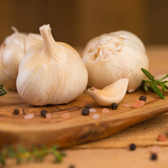 Fresh garlic with spices on a wooden background, thyme and rosemary. Culinary background, ingredients for marinade, close up. Square frame